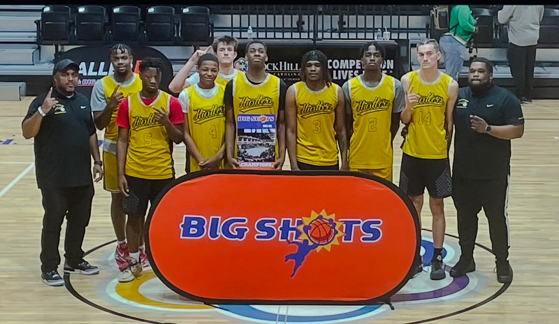 Hustlers-Elite-Boys-Basketball Hustlers Traveling Boys Basketball Team in yellow uniforms standing in front of a "Big Shots" sign
